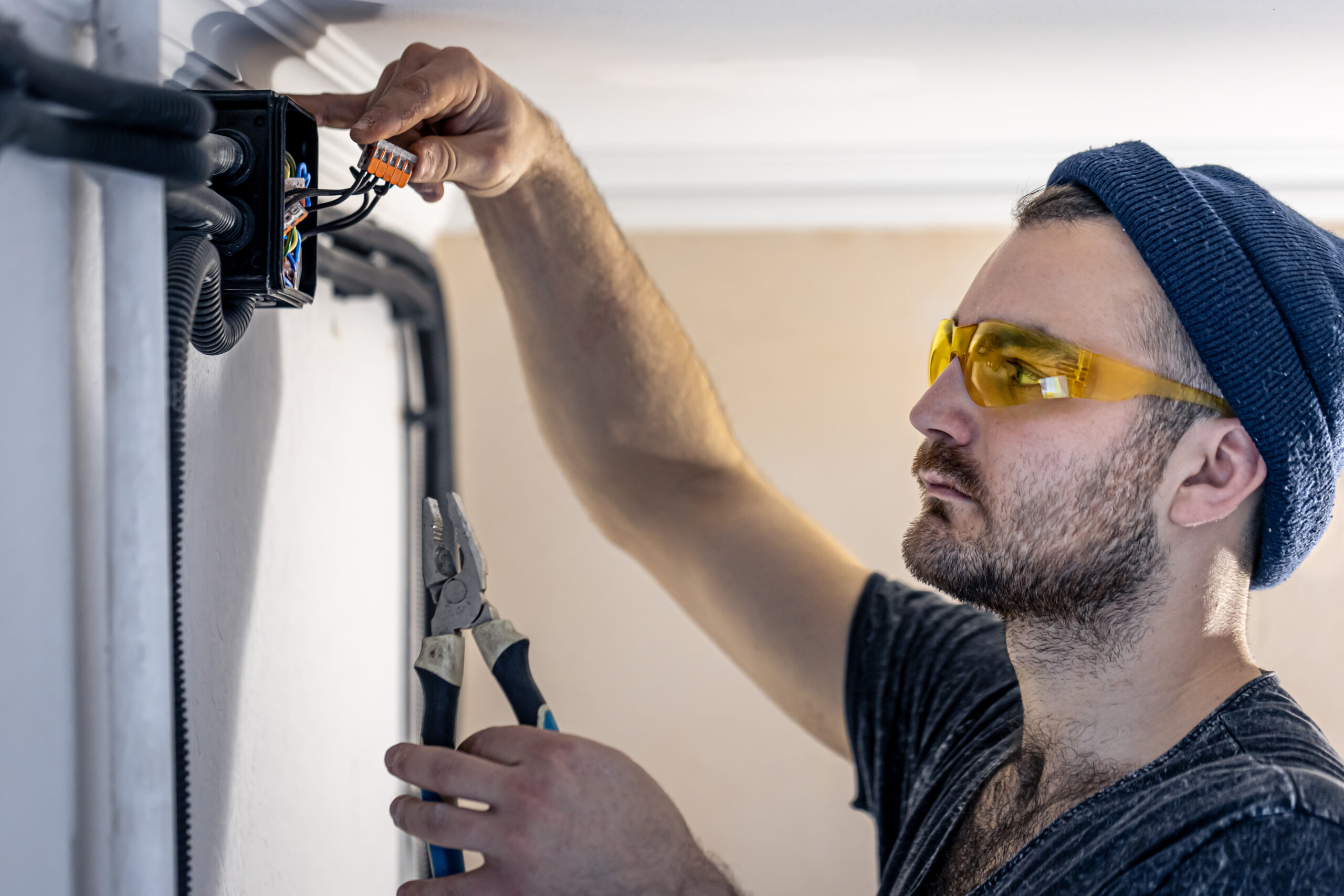 An electrician is mounting electric sockets on the white wall indoors.